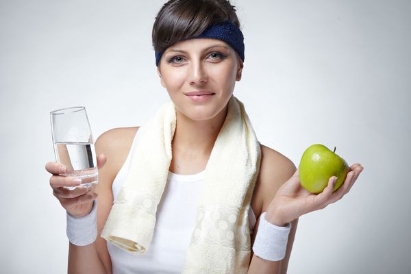 یک زن جوان زیبا و اسپرت در حال نوشیدن آب معدنی و نگه داشتن سیب