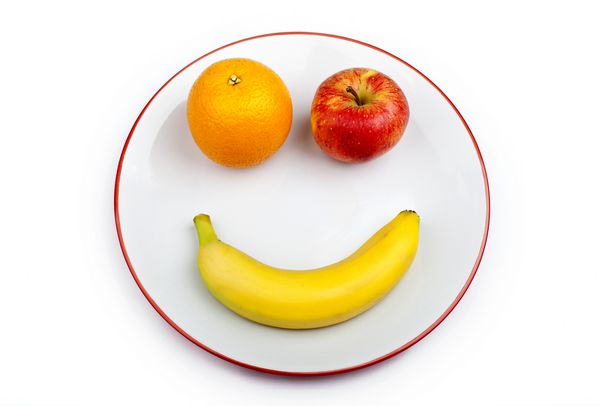 سه قطعه مختلف میوه که چهره ای خندان را بر روی یک بشقاب بیش از یک زمینه سفید تشکیل می دهند