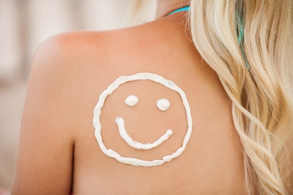 لوسیون ضد آفتاب روی پوست زن برنزه ساخته شده به عنوان صورت خندان