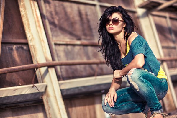 زن زیبا جوان در عینک آفتابی که پشت دیوار بافت نشسته است