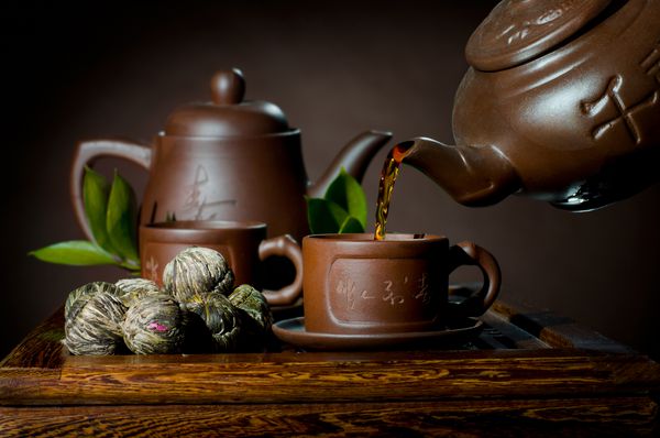 عکس افقی جریان چای قوری گل رس در فنجان بر روی زمینه قهوه ای مراسم چای