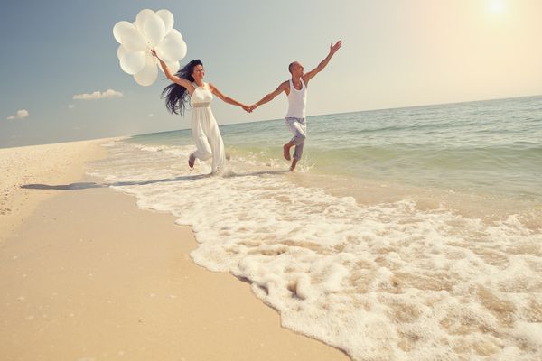 عروس و دامادی که در آفتاب در یک ساحل زیبا گرمسیری مشغول دویدن هستند