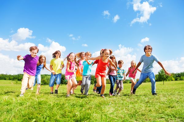 گروه بزرگی از بچه ها دوستان پسران و دختران در روز تابستان آفتابی با لباس های گاه به گاه در پارک در حال دویدن هستند