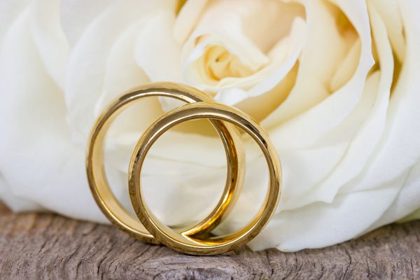 حلقه های عروسی طلایی با گل رز در پس زمینه