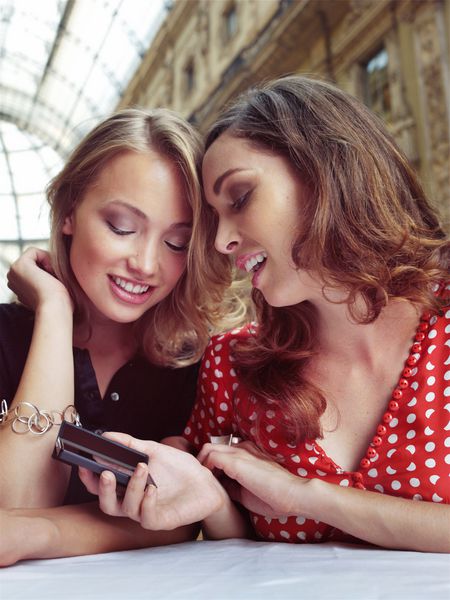دو دوست دختر به تلفن های همراه در کافه نگاه می کنند
