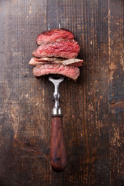 برش های استیک گوشت گاو در چنگال گوشت در زمینه چوبی
