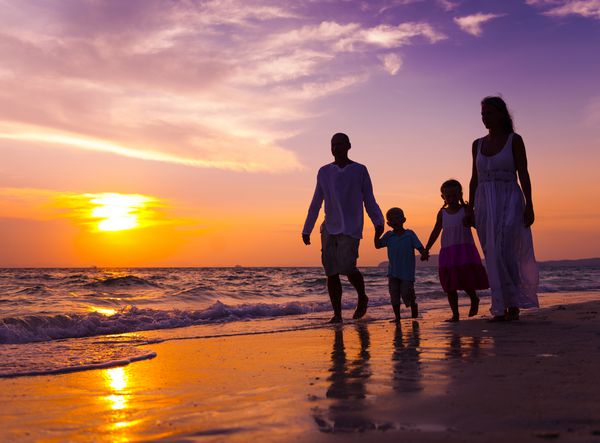 خانواده ای که در غروب آفتاب در ساحل قدم می زنند