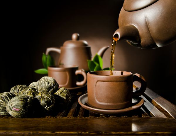 عکس عمودی جریان چای قوری گل رس در فنجان بر روی زمینه قهوه ای مراسم چای