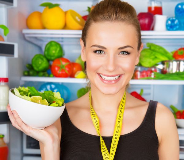 پرتره closeup از یک زن لبخند ناز با نوار اندازه گیری و سالاد سبزیجات تازه مربی ورزشی غذای ارگانیک مفهوم مراقبت از سلامتی و زیبایی