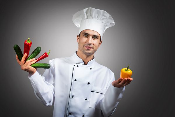 پرتره خنده دار از یک سرآشپز با سبزیجات در دستانش که به دوربین نگاه می کند