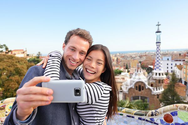 زوج مسافرتی که از عکس سلفی خود با تلفن هوشمند در پارک گوئل بارسلونا اسپانیا هستند صحبت می کنند زن و شوهر جوان و چند چهره زیبا که در حال عکاسی از دوربین هستند که با تلفن هوشمند عاشق لبخند هستند