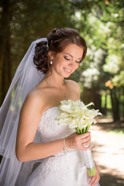 عروس زیبا در لباس عروسی و دسته گل عروس زن تازه متولد شده با گلهای عروسی زن با آرایش عروسی و مدل مو عروس جوان زرق و برق دار در خارج از منزل عروس منتظر داماد است عروس
