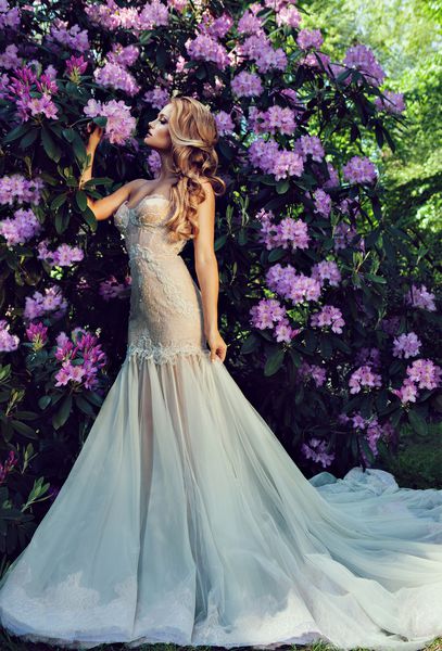 عروس زیبا با لباس مجلل عروسی در باغ با شکوفه های زیبا
