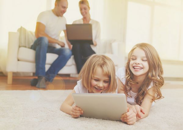 خانواده کودکان فناوری و مفهوم خانه خواهر خندان با رایانه لوحی رایانه های شخصی و والدین در پشت با لپ تاپ