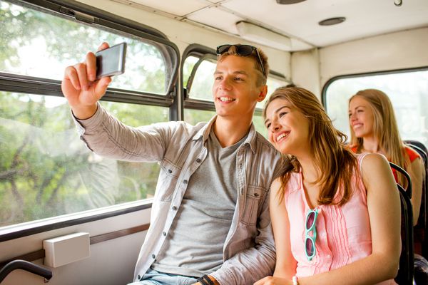 دوستی مسافرت تعطیلات تابستانی مفهوم فناوری و افراد لبخند زن و شوهر با گوشی های هوشمند که با اتوبوس تور مسافرت می کنند و سلفی می کنند