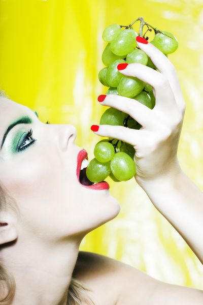 پرتره زن زیبا با آرایش رنگارنگ و پس زمینه خوردن انگور