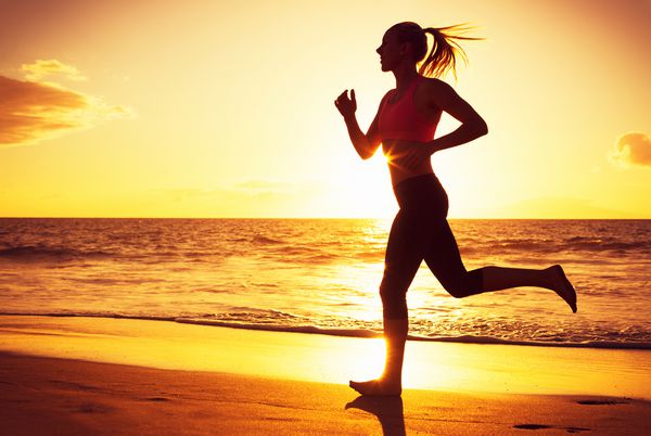 زنی که هنگام غروب آفتاب در ساحل در حال دویدن است