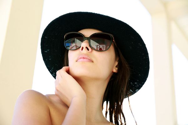 پرتره یک زن زیبا در کلاه و عینک آفتابی که به دور از خانه نگاه می کند