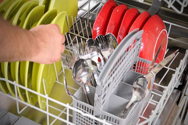 بسته شدن دست های مردانه در حال بارگذاری ظرف های کثیف به ماشین لباسشویی