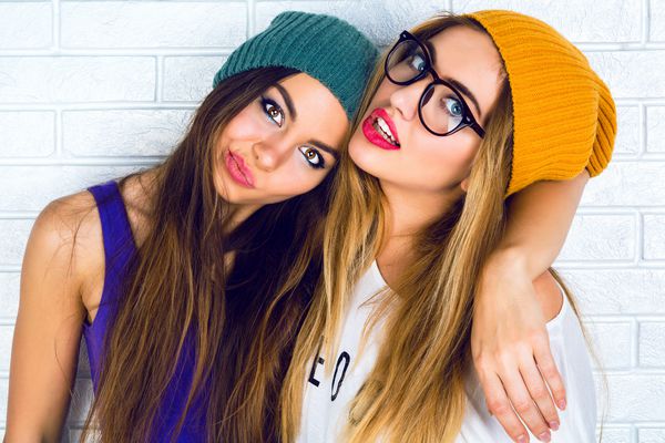 پرتره مد را ببندید و دو دختر زیبا و جوان hipster را با پوشیدن کلاه و عینک روشن تشکیل دهید پرتره استودیویی از دو خواهر شاد بهترین دوستان که از آن لذت می برند و چهره های خنده دار ایجاد می کنند