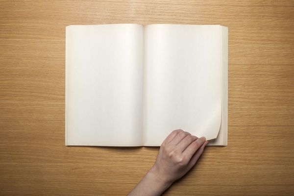 یک دست زن یک کتاب پرنعمت قدیمی یادداشت دفتر خاطرات پخش کرده و از طریق صفحات کتاب روی میز چوبی نمای بالا در استودیو نگه می دارد