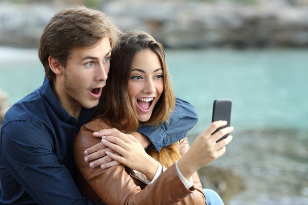 زوج شوکه شده هنگام تماشای تلفن هوشمند در تعطیلات ساحل