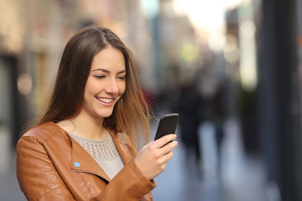 زن مبارک با استفاده از تلفن هوشمند در خیابان با پیش زمینه روشن و تمیز