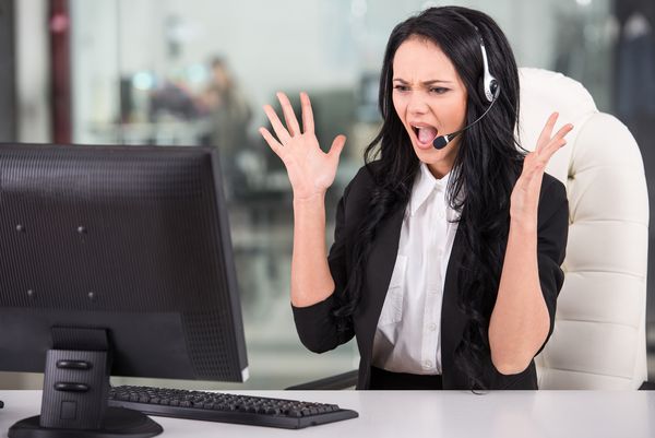 زن عاطفی هنگام کار روی رایانه خود در مرکز تماس با تلفن صحبت می کند