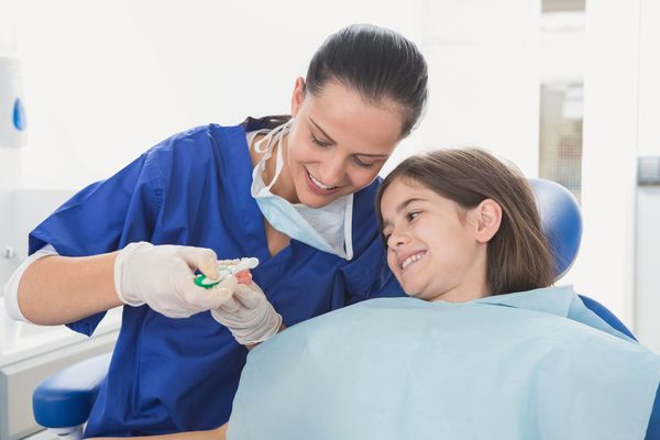 دندانپزشک کودکان در مورد نحوه استفاده از مسواک در کلینیک دندانپزشکی به بیمار جوان توضیح می دهد