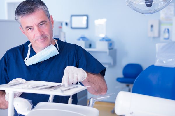 ابزار جمع آوری دندانپزشک و لبخند زدن در دوربین در کلینیک دندانپزشکی