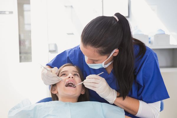 دندانپزشک کودکان با استفاده از کاوشگر دندانپزشکی و آینه زاویه دار در دهان باز بیمار