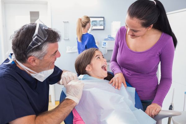 لبخند دندانپزشک کودکان با یک بیمار جوان و مادرش در کلینیک دندانپزشکی