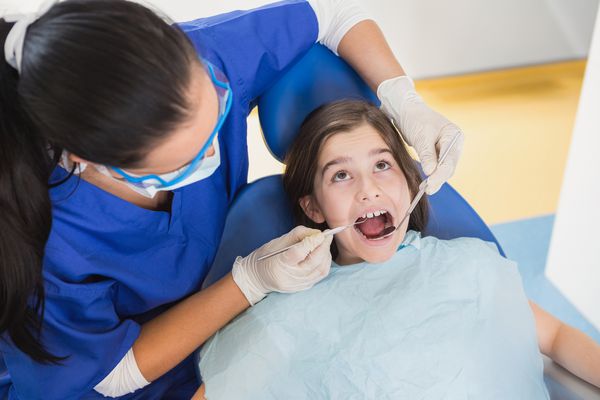 دندانپزشک کودکان در معاینه بیمار خود را با دهان باز در کلینیک دندانپزشکی معاینه می کند