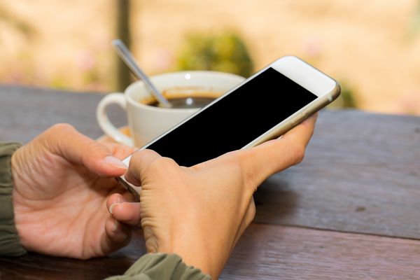 کلوزآپ زن که دارای تلفن همراه در مقابل جام قهوه است