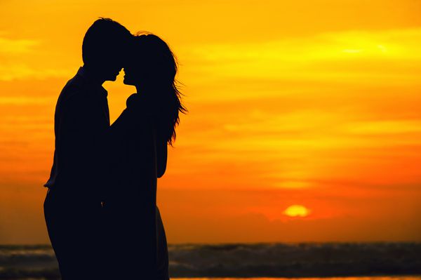زن و شوهر عاشقانه در ساحل در غروب خورشید رنگارنگ در پس زمینه