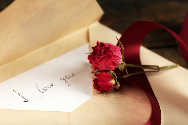پاکت نامه ای با نامه عشق روبان و گل رز خشک شده بر روی زمینه میز چوبی روستایی