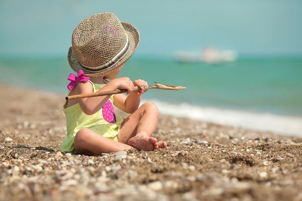 دخترک در کلاه نشسته در ساحل و به دریا نگاه می کند