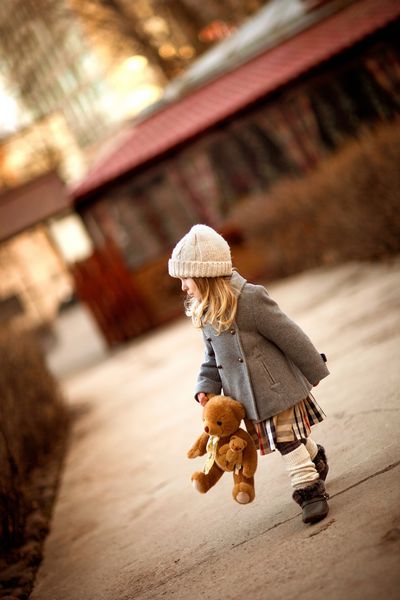 دختر کوچکی که با یک خرس عروسکی در دستش قدم می زند
