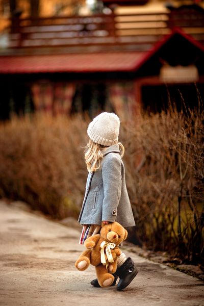 دختر کوچکی که با یک خرس عروسکی در دستش در باغ قدم می زند