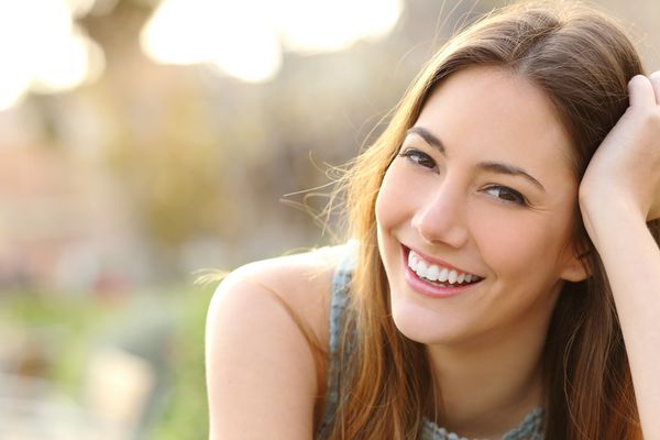 زنی که با لبخند کامل و دندانهای سفید در یک پارک لبخند می زند و به دوربین نگاه می کند