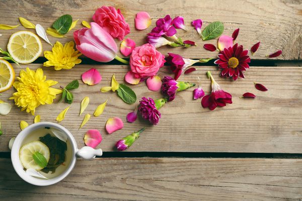 فنجان چای گیاهی با گلهای زیبا روی زمینه چوبی