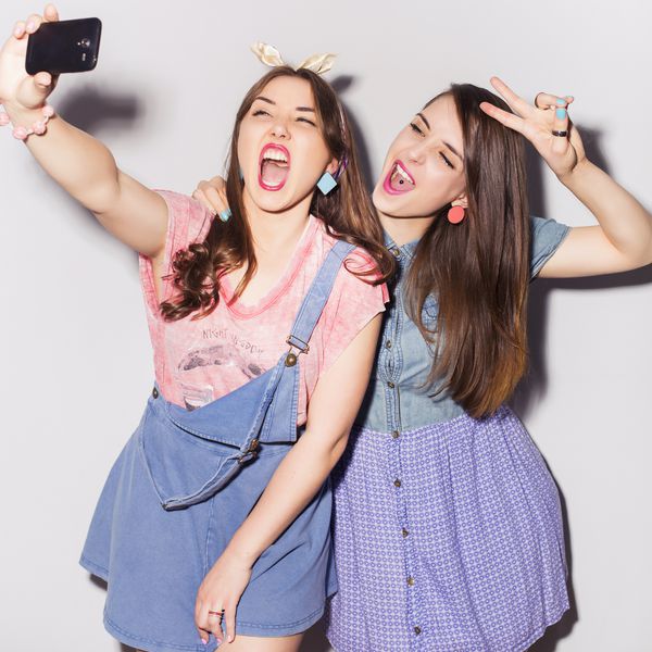 دو دختر دختر نوجوان زیبا که در کنار هم می گذرانند برای سرگرمی چهره های خنده دار سلفی درست می کنند لباس شلوار جین