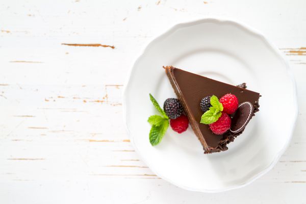 کیک شکلاتی با تمشک توت سیاه نعناع بشقاب سفید پس زمینه چوب سفید نمای بالا