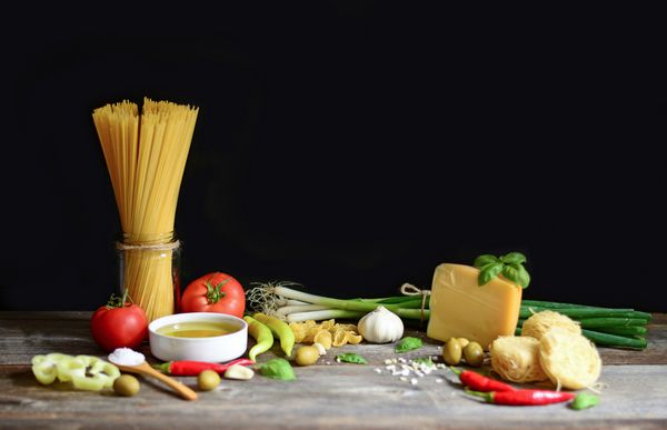 مواد غذایی ایتالیایی و مدیترانه ای در زمینه چوبی قدیمی اسپاگتی زیتون ریحان گیلاس گوجه فرنگی ماکارونی سیر فلفل و زیتون