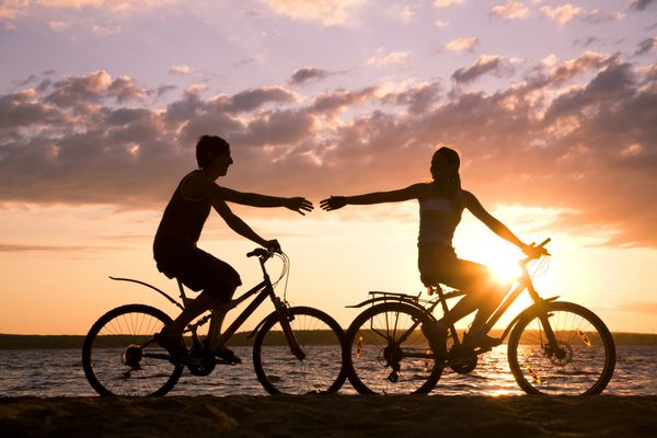 شبح های زوج خوشبختی که هنگام غروب دوچرخه در ساحل در هنگام غروب آفتاب دست به یکدیگر می کشند