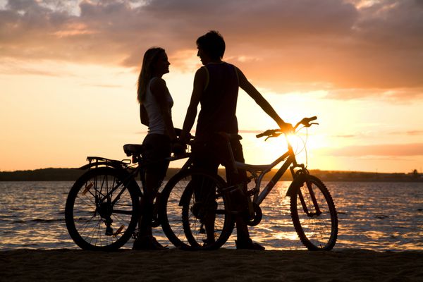 زن و شوهر جوان با دوچرخه خود در ساحل ایستاده و به یکدیگر نگاه می کنند