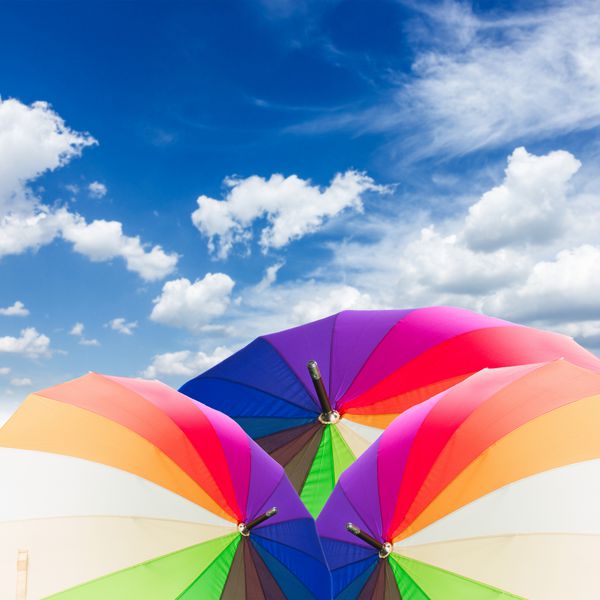 چترهای رنگین کمان را بر فراز آسمان آبی با ابرها باز کنید
