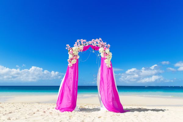عروسی در ساحل قوس عروسی به رنگ بنفش تزئین شده با گل در ساحل شن گرمسیری