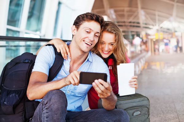 زن و شوهر در فرودگاه با استفاده از برنامه سفر از طریق تلفن های هوشمند