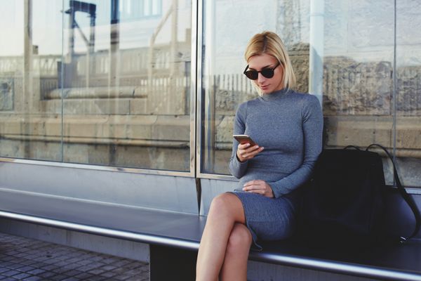زن جوان با نگاه مرسوم مدام اطلاعات تلفن را در حالی که منتظر بیرون از خانه در تاکسی خود هستید توریستی زن شیک با استفاده از تلفن همراه برای مشاهده نقشه شهر به صورت آنلاین در هنگام نشستن در ایستگاه اتوبوس